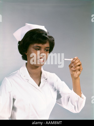 Anni sessanta americano africano donna INFERMIERA IN UNIFORME DI TERMOMETRO A LETTURA Foto Stock