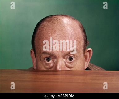 Anni sessanta BALDING MAN PEEKING SU DESKTOP CON solo la metà superiore della testa che mostra Foto Stock