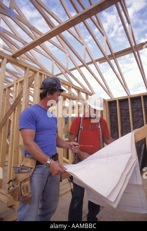 Operaio edile esaminando i piani mentre si lavora sul telaio in legno home in costruzione NW Washington Foto Stock