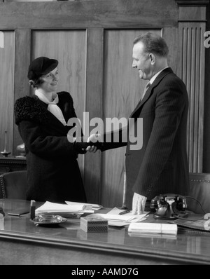1930s uomo stringono le mani con la donna alla scrivania in ufficio Foto Stock