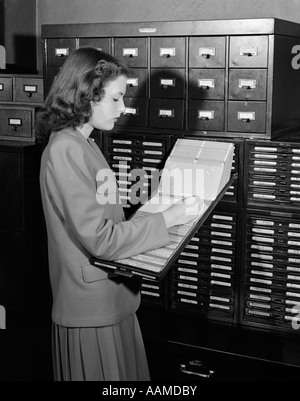 Negli anni quaranta anni cinquanta DONNA IN UFFICIO in piedi vicino armadietti Foto Stock