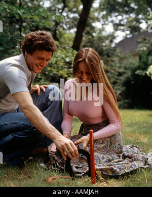 1970 anni settanta GIOVANE UOMO DONNA ALL'APERTO CANTIERE PRATO estate giocando ferri di cavallo attività di gioco retrò Foto Stock