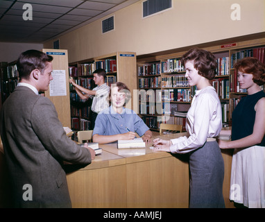 Anni sessanta TEEN STUDENTI IN LIBRERIA AL MOMENTO DEL CHECK OUT DESK pile scaffali di libri di riferimento di studio Foto Stock