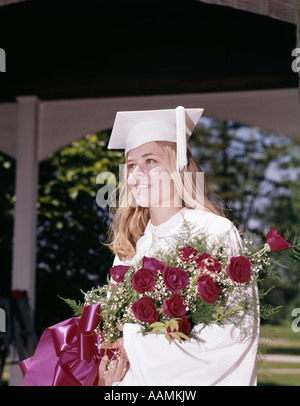 Anni sessanta Ritratto di giovane donna laureata in tappo bianco e camice azienda bouquet di rose OUTDOOR Foto Stock