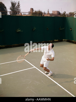 1970 anni settanta retrò uomo giocando a tennis Racchetta oscillante per colpire la sfera di azione esercizio di ricreazione Foto Stock