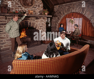 Anni sessanta tre coppie UOMINI DONNE IN SKI LODGE PER PIETRA camino fuoco parlando a suonare la chitarra Vacanza Ferie Foto Stock