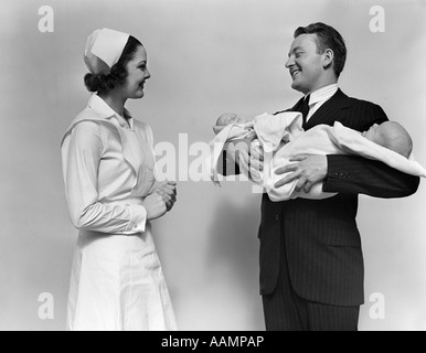 1930s 1940s donna sorridente infermiera a parlare con l'uomo nuovo fiero padre tenendo il Neonato Neonati TWIN Foto Stock