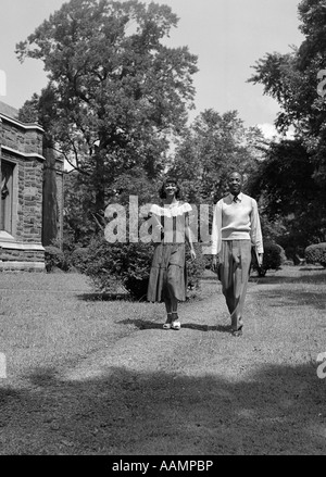 Negli anni quaranta anni cinquanta African American College giovane camminando sul campus il trasporto di libri Foto Stock