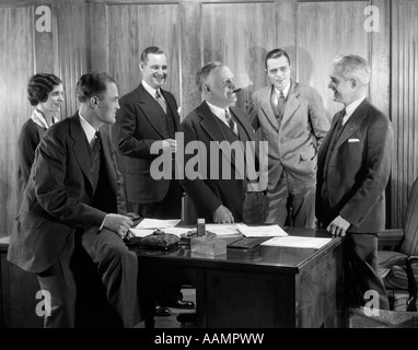 1930 Ufficio sorridente gruppo quattro uomini una donna boss di fumare il sigaro parlando incontro quinto uomo Foto Stock