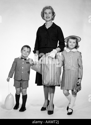 Anni Cinquanta anni sessanta donna madre di due bambini ragazza ragazzo Holding Hands SHOPPING BAG vestito figlio Pantaloncini Pantaloni figlia del palloncino HAT GONNA Foto Stock