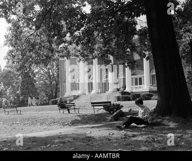 Anni sessanta collegio femminile studente seduto sotto agli alberi a studiare con edificio del campus & ALTRI STUDENTI A PIEDI IN BACKGROUND Foto Stock