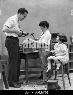 1920s PADRE DI FAMIGLIA CARPENTER insegnamento figlio e figlia di costruire una casetta per uccelli CON STRUMENTI PER LA LAVORAZIONE DEL LEGNO Foto Stock