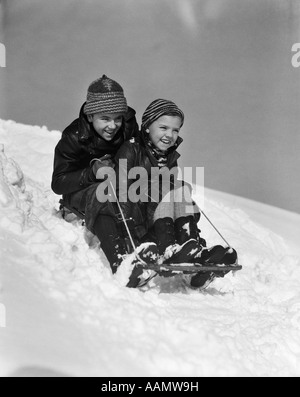 1930s ragazzo e ragazza di andare in discesa in slitta al di fuori nella neve Foto Stock