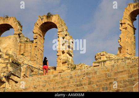 Femmina passeggiate turistiche fino a gradini area salotto verso rovinato arcate del vecchio Colosseo romano di El Jem tunisia Foto Stock