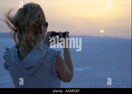 Capelli biondi turista femminile scatta una fotografia del sorgere del sole sopra le saline chott el djerid tunisia Foto Stock