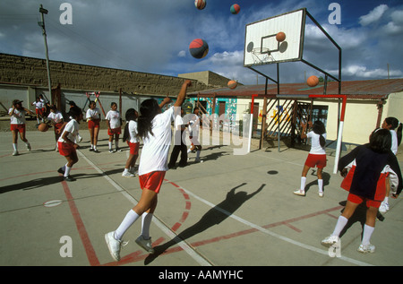 Ragazze Sparare hoops sulla loro scuola s campi da tennis all'aperto durante l'educazione fisica classe a Oruro Bolivia Foto Stock