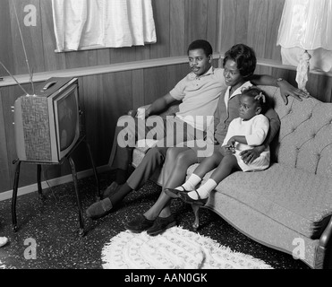 Anni Settanta famiglia americana africana guardando la televisione portatile madre padre ragazza seduta SUL LETTINO Foto Stock