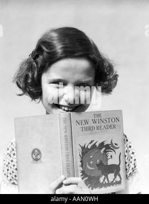 1930s sorridente ragazza con i capelli BOBBED tenendo aperta la terza elementare LIBRO DI LETTURA Foto Stock