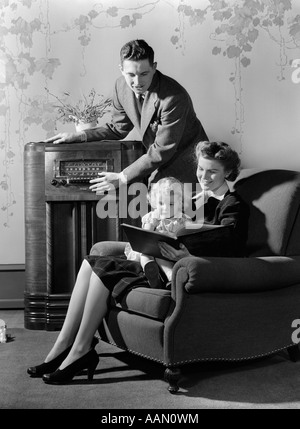 1930s 1940s famiglia ascoltando la radio mentre la madre legge libro per bambina seduti in grembo in poltrona Foto Stock