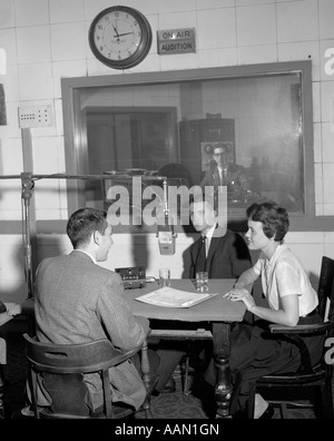 Anni sessanta disc jockey ALLA STAZIONE RADIO MICROFONO MIKE PARLARE CON IL GIOVANE UOMO DONNA A TAVOLA L UOMO NELLA SALA DI CONTROLLO Foto Stock