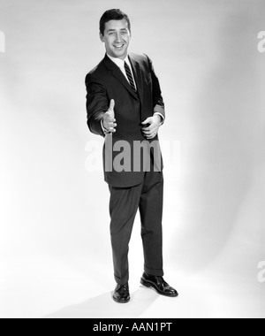 Anni sessanta sorridente a piena lunghezza Ritratto uomo uomo d affari con mano esteso nel messaggio di saluto per stretta di mano Foto Stock