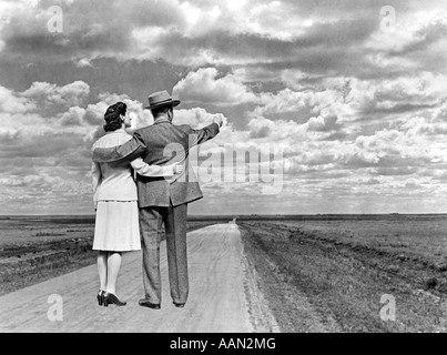 1940s vista posteriore giovane con le braccia intorno a ogni altro permanente sulla strada aperta rivolta all'orizzonte Foto Stock