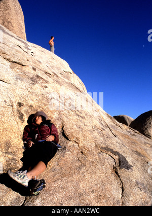 Una donna si siede su una roccia mentre un uomo guarda la vista a Joshua Tree Foto Stock