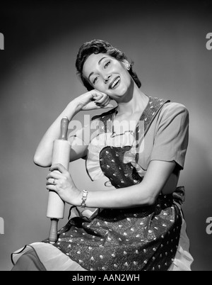 Anni Cinquanta donna casalinga che indossa il grembiule HOLDING MATTARELLO guardando la fotocamera Foto Stock