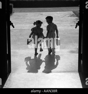 Anni Cinquanta STAGLIANO BOY GIRL Holding Hands lasciando le porte della scuola per andare a casa alla fine della giornata le ombre pomeriggio amici amicizia Foto Stock