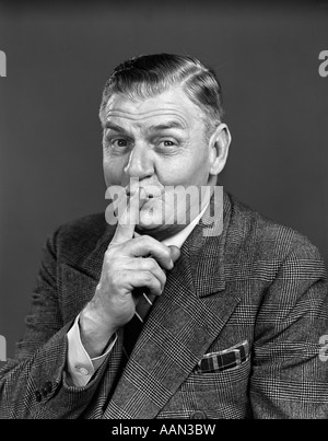 1940s uomo anziano indossare tuta rendendo SHUSH gesto guardando la fotocamera Foto Stock