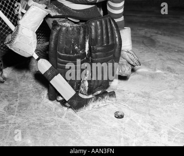 Negli anni quaranta anni cinquanta close-up di imbottitura GOALIE mostrato per la cintura verso il basso tenendo STICK CON PUCK davanti a lui Foto Stock