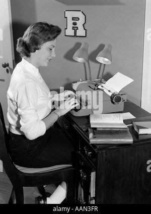 Anni Cinquanta collegio femminile studente seduto alla scrivania digitando guardando il libro accanto a una macchina da scrivere Foto Stock