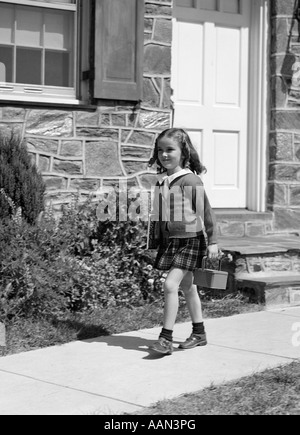 1940s bambina andare a scuola a piedi al di fuori della porta di casa portando scatola di pranzo Foto Stock