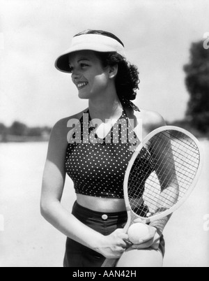 1930s DONNA IN POLKA DOT HALTER TOP SHORTS & VISIERA PARASOLE in possesso di una palla da tennis e delle racchette Foto Stock