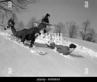 Anni sessanta 3 ragazzi slittino in esecuzione in discesa in neve invernale Foto Stock