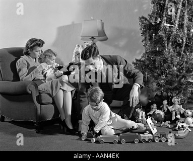 1930s 1940s famiglia ATTORNO AD ALBERO DI NATALE ragazzo giocando con il treno papà aiuta la mamma e la ragazza in sedia Foto Stock