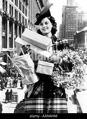 1930s 1940s donna che guarda la fotocamera piena di armi con lo Shopping di Natale pacchetti & corona composito con scene di strada Foto Stock