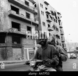 Due uomini su un ciclomotore di equitazione edifici del passato a Beirut, Libano, danneggiato durante la guerra civile Foto Stock