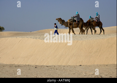I turisti a cavallo di cammelli essendo portato attraverso lo spostamento le dune di sabbia del deserto del Sahara a Douz Tunisia Foto Stock