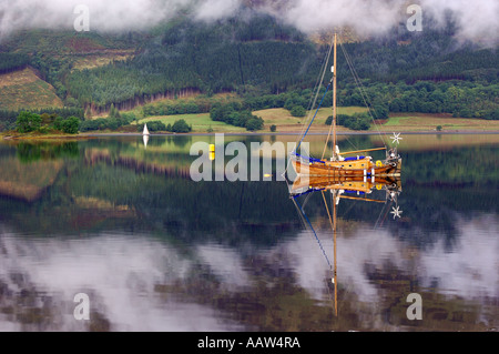 Graziosa costruita tradizionalmente in legno barca a vela ormeggiata su Loch Leven vicino a Ballachulish Glencoe con luce deriva nuvole da Foto Stock