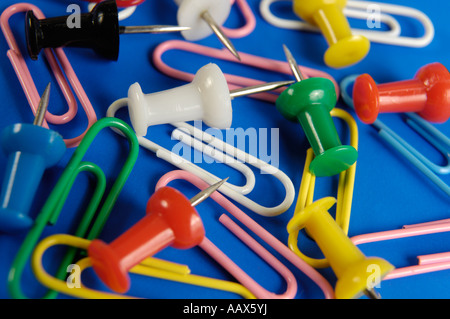 Thumbtacks colorati e graffette su sfondo blu delle forniture di ufficio Foto Stock