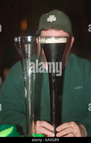 Un colore dell'immagine in verticale di un paffuto uomo caucasico in una felpa verde e shamrock cappuccio nascosto dietro due metà cantiere bicchieri da birra Foto Stock