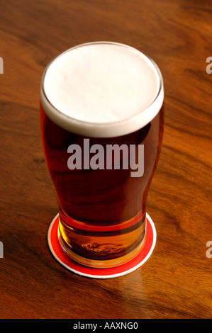 Pieno di pinta di birra su di un tappeto di birra in un pub in legno tabella Foto Stock