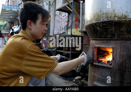 Giovane uomo aggiunta di carbone di legna per una stufa per esterni nel quartiere musulmano di Daqingzhen Si in Xi'an, Shaanxi, Cina. Foto Stock