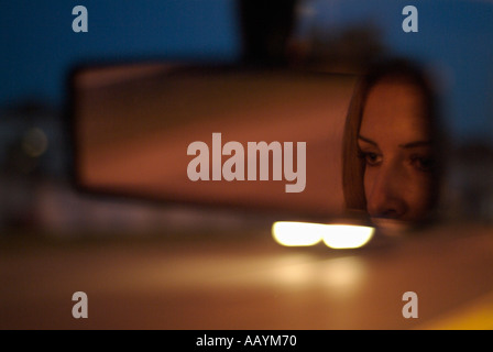 Specchio retrovisore con la riflessione di un volto di donna in un auto guidando lungo una strada di notte Foto Stock