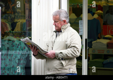 Uomo che legge il giornale mentre in attesa per la moglie su un viaggio di shopping. Foto Stock