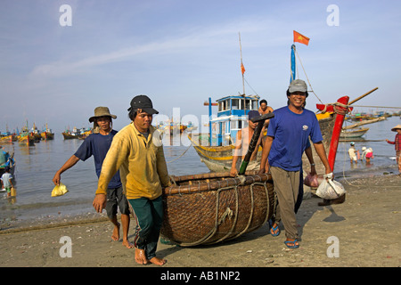 Quattro pescatori portano rotondo piccolo tessuto barca fino beach Lang Chai villaggio di pescatori nei pressi di Mui Ne Vietnam Foto Stock