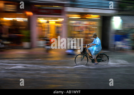 Uomo in pioggia cape corse in bicicletta lungo allagato De Tham Street Pham Ngu Lao district Ho Chi Minh City Vietnam Foto Stock