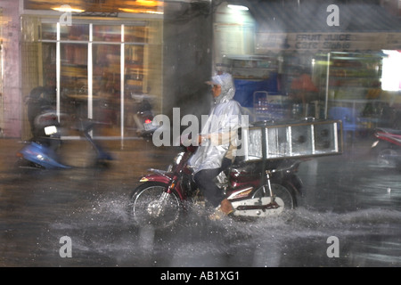 Uomo in plastica impermeabile con moto corse di carico lungo allagato De Tham Street Pham Ngu Lao district Ho Chi Minh City Vietnam Foto Stock