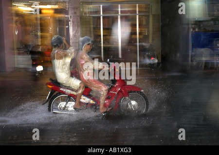 Due donne in pioggia capes ride motociclo su allagato De Tham Street Pham Ngu Lao district Ho Chi Minh City Vietnam Foto Stock